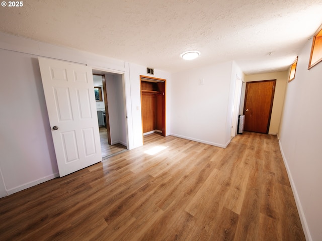 unfurnished bedroom featuring light wood-type flooring, a textured ceiling, baseboards, and a closet