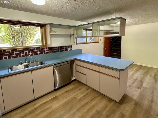 kitchen featuring dishwasher, a sink, light wood-type flooring, a textured ceiling, and tasteful backsplash