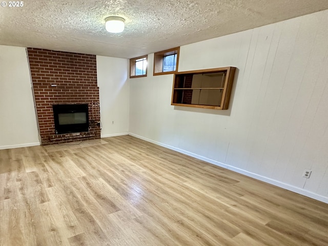 unfurnished living room featuring wood finished floors, a textured ceiling, a brick fireplace, and baseboards
