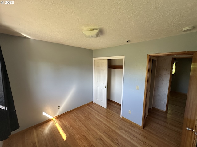 unfurnished bedroom with wood finished floors, a closet, baseboards, and a textured ceiling