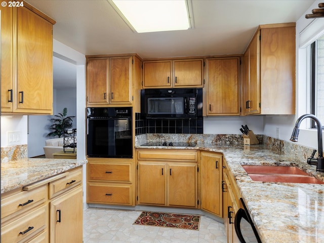 kitchen featuring light stone counters, a sink, and black appliances