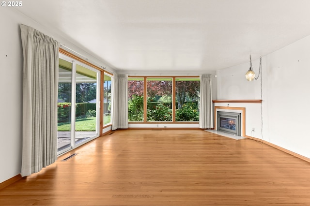 unfurnished living room with wood finished floors, plenty of natural light, and a fireplace with flush hearth