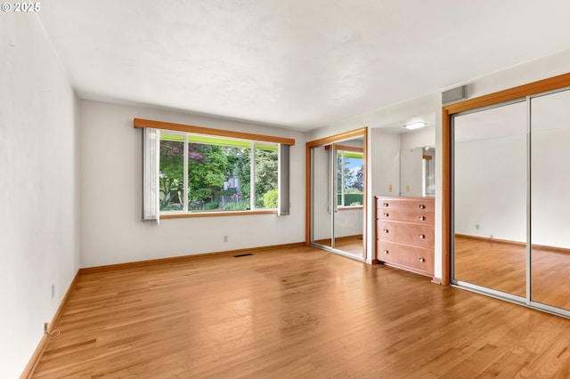 unfurnished bedroom with two closets, light wood-style flooring, and baseboards