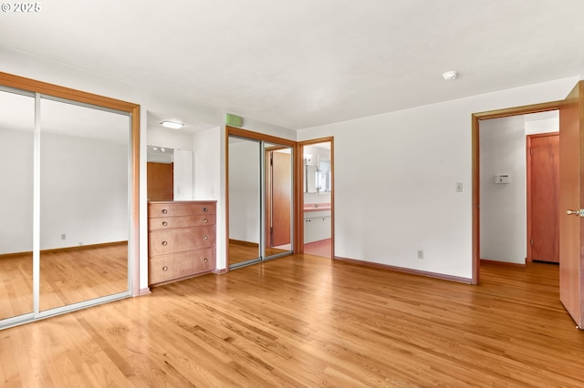 unfurnished bedroom with multiple closets, light wood-type flooring, baseboards, and ensuite bathroom