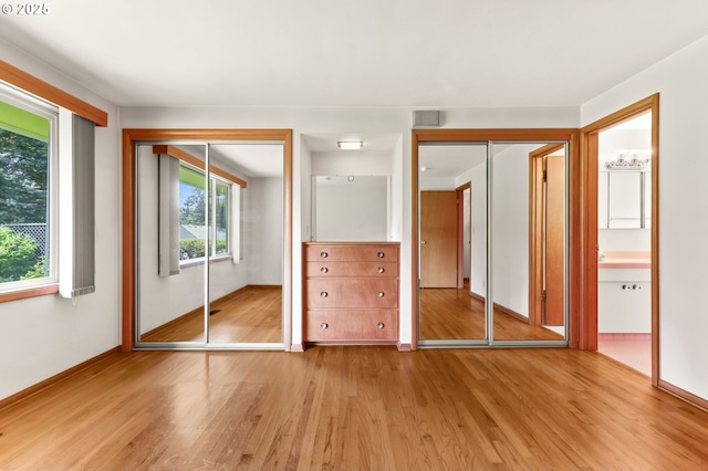 unfurnished bedroom with wood finished floors, baseboards, multiple closets, and connected bathroom