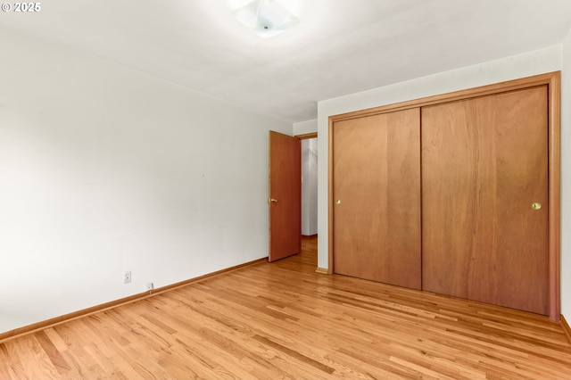unfurnished bedroom featuring light wood-style floors, baseboards, and a closet