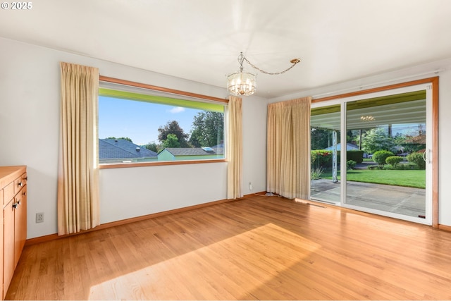 unfurnished dining area with a chandelier, light wood-type flooring, and baseboards
