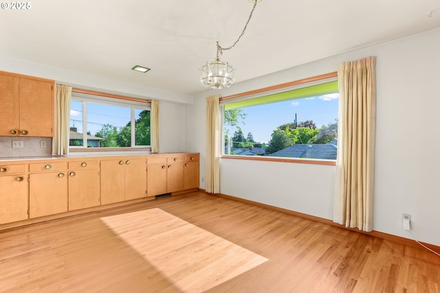 unfurnished dining area with a chandelier, light wood-style flooring, and healthy amount of natural light
