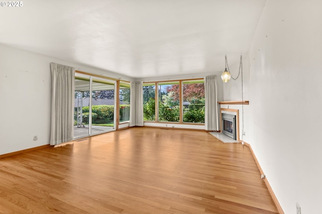 unfurnished living room featuring plenty of natural light, light wood finished floors, and a fireplace with flush hearth