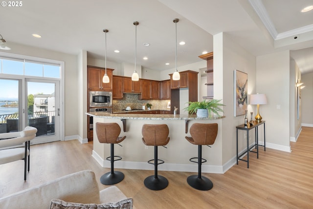 707 N Hayden Island Dr Unit 415, Portland, OR 97217 - kitchen with appliances with stainless steel finishes, brown cabinetry, light wood-type flooring, light stone counters, and a peninsula