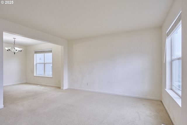 empty room featuring light carpet, baseboards, and an inviting chandelier