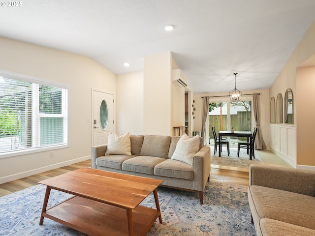 living area featuring an inviting chandelier, lofted ceiling, a wall mounted AC, and light wood finished floors