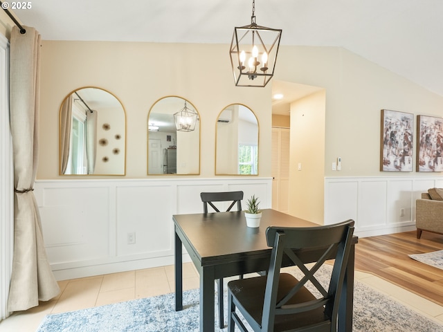 dining room with an inviting chandelier, a wainscoted wall, a decorative wall, and lofted ceiling