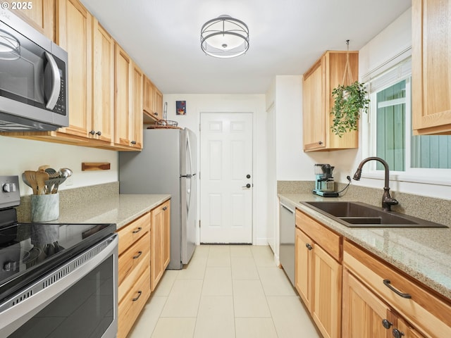 kitchen with a sink, light tile patterned floors, light stone counters, light brown cabinets, and stainless steel appliances
