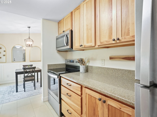 kitchen featuring light brown cabinetry, light stone countertops, hanging light fixtures, appliances with stainless steel finishes, and light tile patterned floors