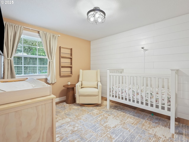 bedroom featuring wooden walls, baseboards, a nursery area, and wood finished floors