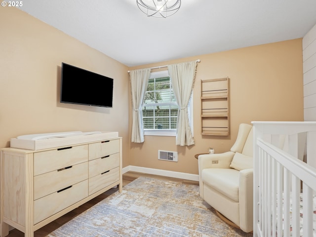 bedroom featuring a nursery area, baseboards, and wood finished floors