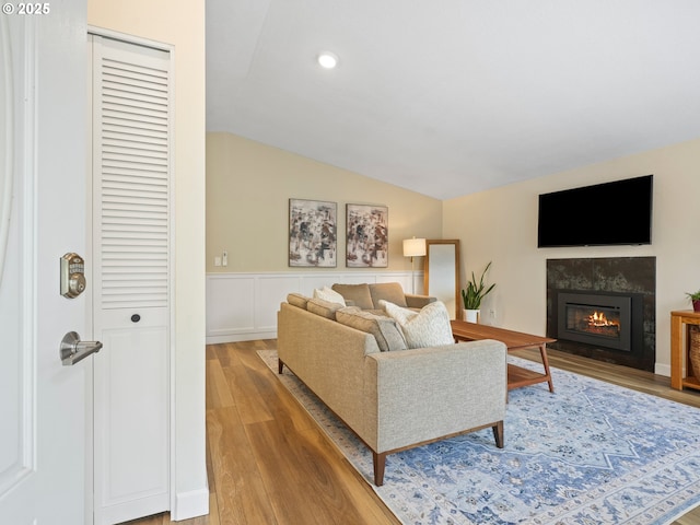 living room featuring a glass covered fireplace, light wood-style floors, recessed lighting, a wainscoted wall, and vaulted ceiling