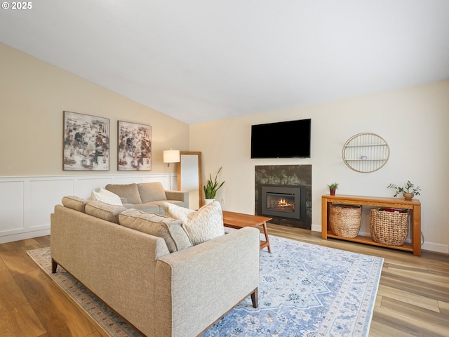 living room with a glass covered fireplace, wood finished floors, and lofted ceiling