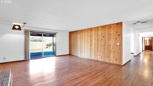 unfurnished room featuring hardwood / wood-style flooring, wooden walls, and a textured ceiling