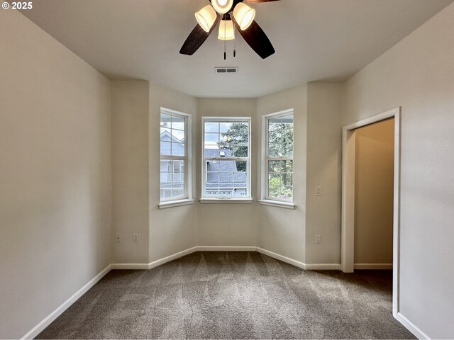 carpeted empty room featuring plenty of natural light, a ceiling fan, baseboards, and visible vents