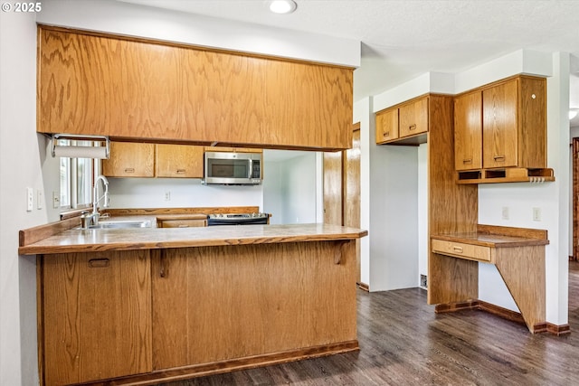 51945 SW Creekview Pl, Scappoose, OR 97056 - kitchen featuring stainless steel appliances, a sink, dark wood-style flooring, a peninsula, and brown cabinetry