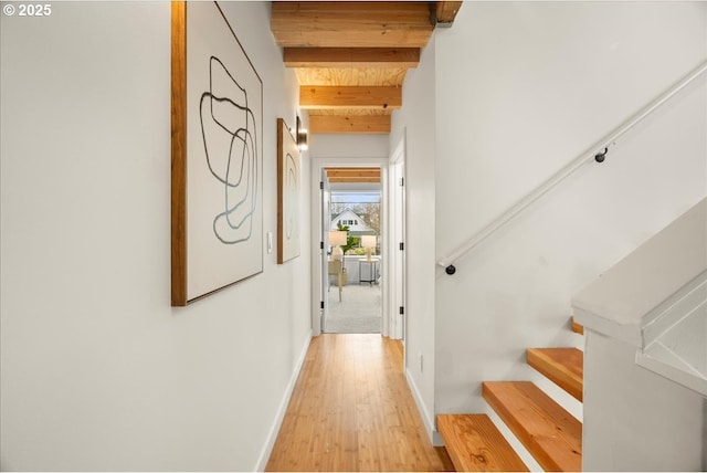 hallway featuring baseboards, light wood finished floors, beam ceiling, and stairs