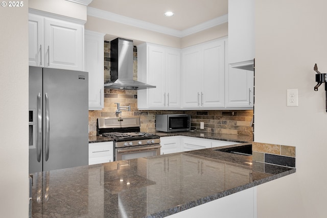 kitchen featuring appliances with stainless steel finishes, white cabinetry, dark stone countertops, a peninsula, and wall chimney exhaust hood