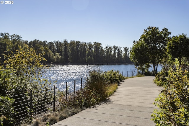 view of dock with a water view, fence, and a forest view