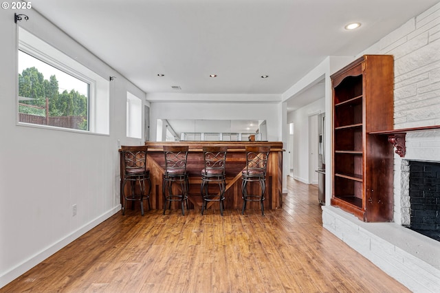 dining room with a bar, a brick fireplace, baseboards, wood finished floors, and recessed lighting