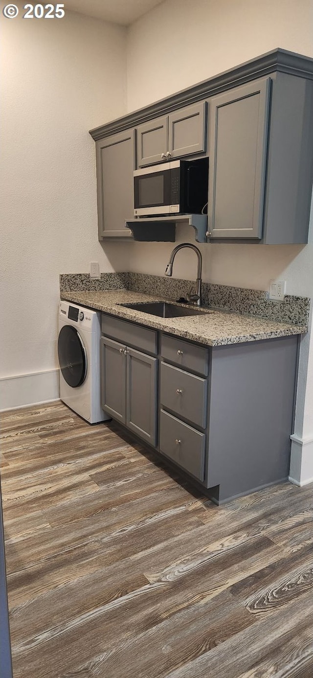 kitchen featuring washer / dryer, gray cabinets, dark wood-type flooring, and baseboards