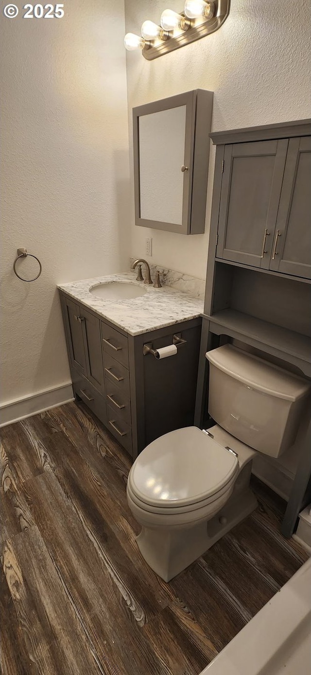 bathroom with toilet, wood finished floors, vanity, and baseboards