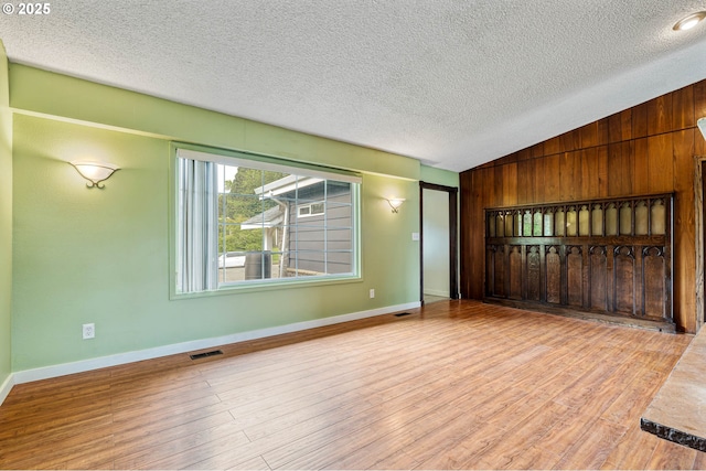unfurnished living room with vaulted ceiling, a textured ceiling, wood finished floors, baseboards, and wood walls