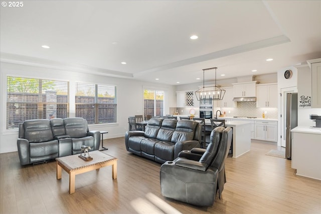 living room with recessed lighting, a raised ceiling, and light wood-type flooring