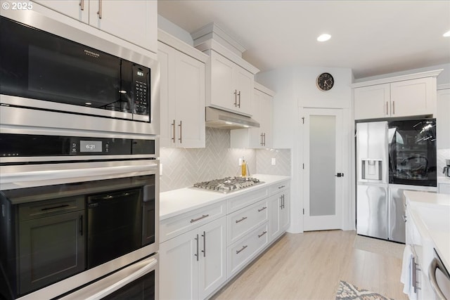 kitchen with white cabinets, under cabinet range hood, stainless steel appliances, light countertops, and tasteful backsplash
