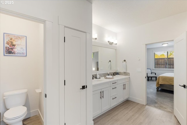 ensuite bathroom with double vanity, wood finished floors, toilet, baseboards, and ensuite bathroom