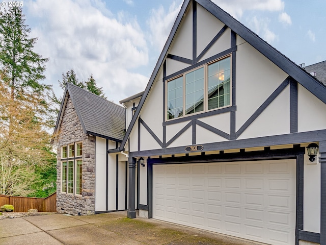 tudor-style house featuring driveway, stone siding, fence, and stucco siding