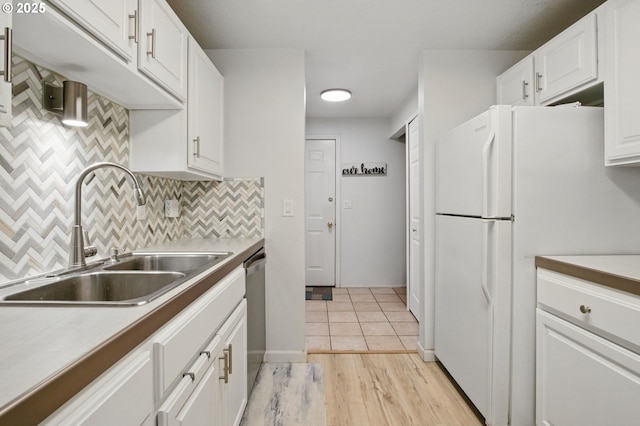 kitchen with a sink, freestanding refrigerator, white cabinetry, stainless steel dishwasher, and backsplash