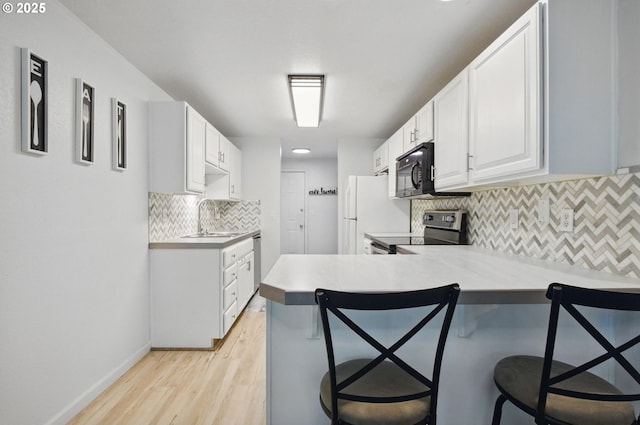 kitchen featuring stainless steel appliances, a sink, a breakfast bar, light wood-style floors, and tasteful backsplash