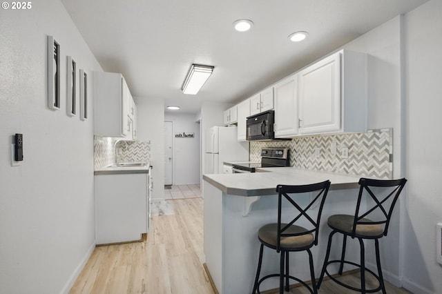 kitchen featuring stainless steel range with electric stovetop, black microwave, a sink, freestanding refrigerator, and a breakfast bar area