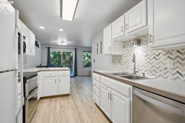 kitchen featuring appliances with stainless steel finishes, a sink, light wood-style floors, white cabinets, and decorative backsplash