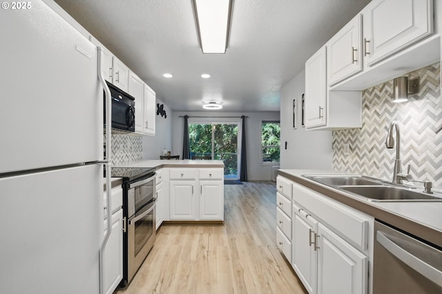 kitchen featuring appliances with stainless steel finishes, a sink, light wood-style floors, decorative backsplash, and white cabinets
