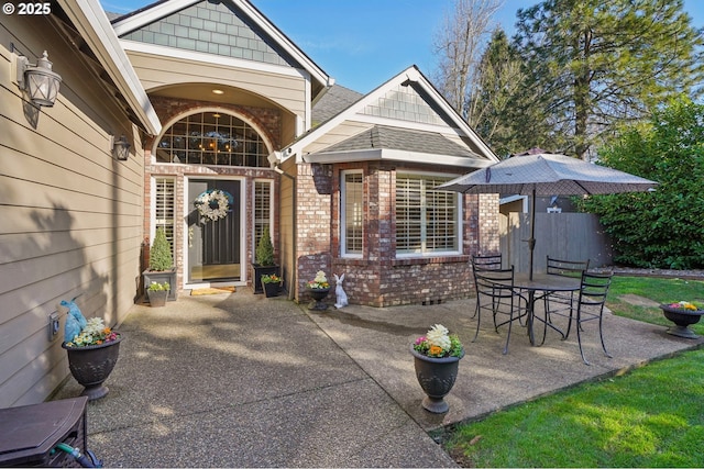 entrance to property with brick siding, roof with shingles, and a patio area