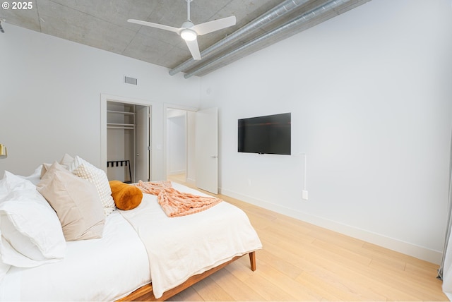 bedroom with light wood-style flooring, a ceiling fan, a towering ceiling, baseboards, and a closet