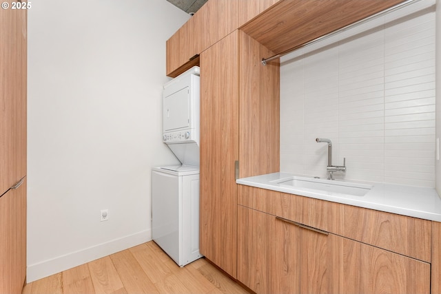 laundry room with laundry area, light wood finished floors, baseboards, stacked washing maching and dryer, and a sink