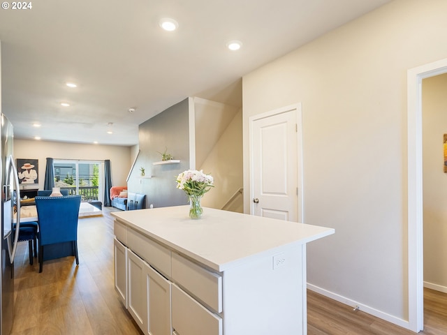 kitchen with recessed lighting, wood finished floors, a kitchen island, white cabinets, and light countertops