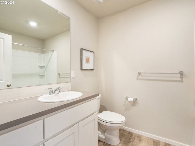 full bath featuring toilet, wood finished floors, vanity, baseboards, and walk in shower