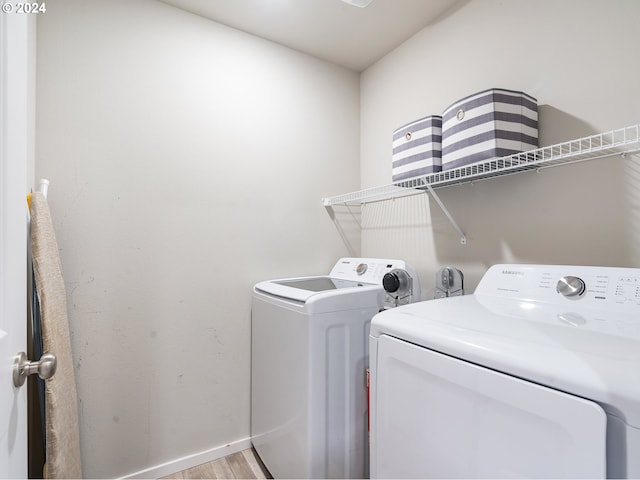 clothes washing area with laundry area, light wood-type flooring, washing machine and clothes dryer, and baseboards