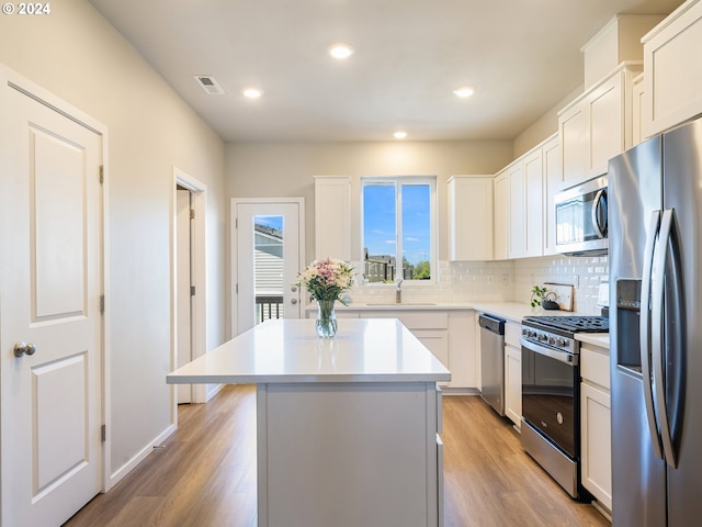 kitchen with a center island, light wood finished floors, stainless steel appliances, visible vents, and decorative backsplash