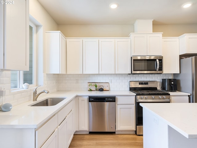 kitchen with appliances with stainless steel finishes, a sink, white cabinets, and decorative backsplash